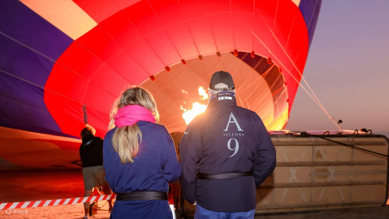 Para penumpang menyaksikan dengan penuh harap saat balon udara mengembang, bersiap untuk lepas landas