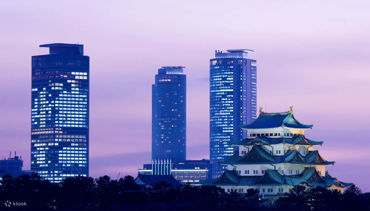 名古屋城在黄昏时分点上灯光，背景是现代摩天大楼，展示日本名古屋传统与现代建筑的融合