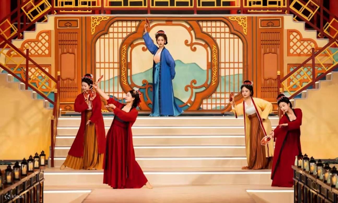 Auf der Bühne führen mehrere Tänzer in farbenprächtigen, historischen Kostümen anmutige Bewegungen auf. Die chinesische Dekoration und die Laternen im Hintergrund unterstreichen das klassische Ambiente.