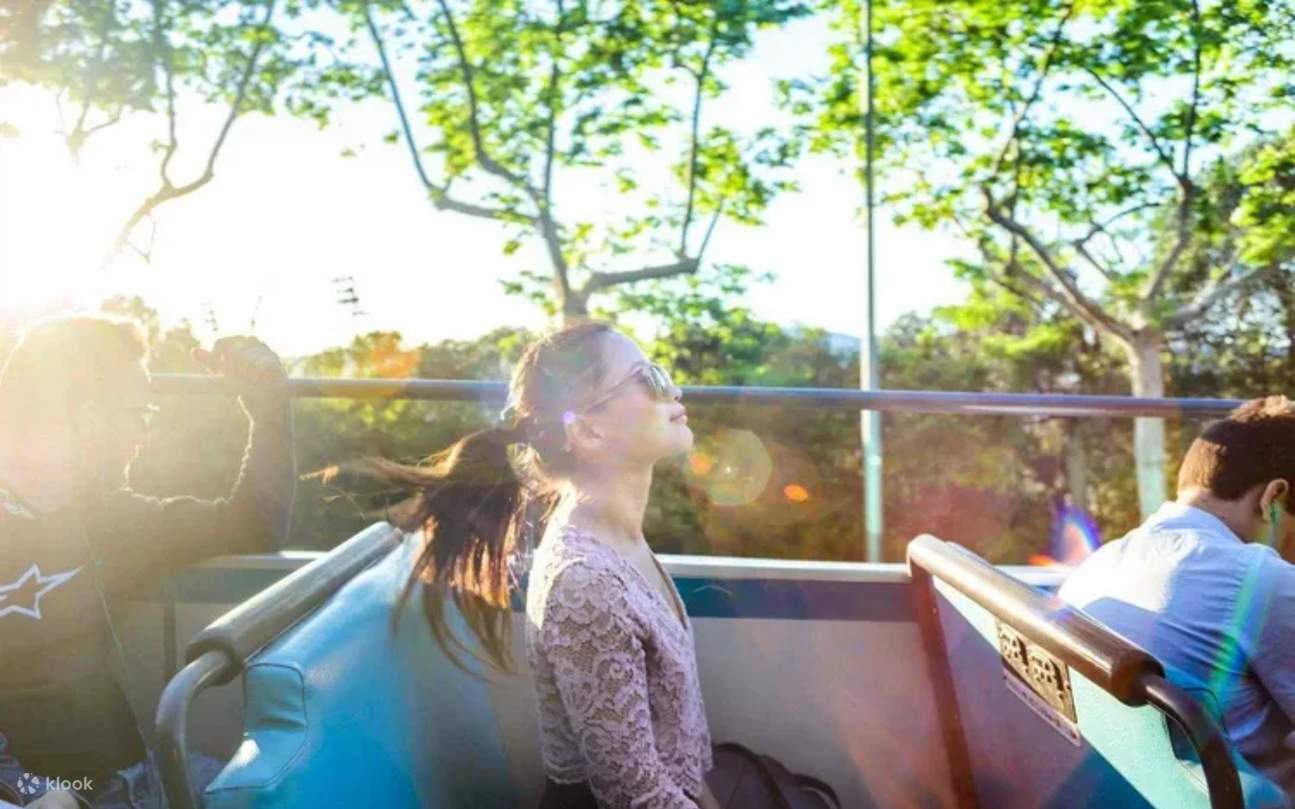 Penumpang bersantai, menikmati suasana terbuka yang menyegarkan sambil menjelajahi lanskap perkotaan Barcelona yang ramai