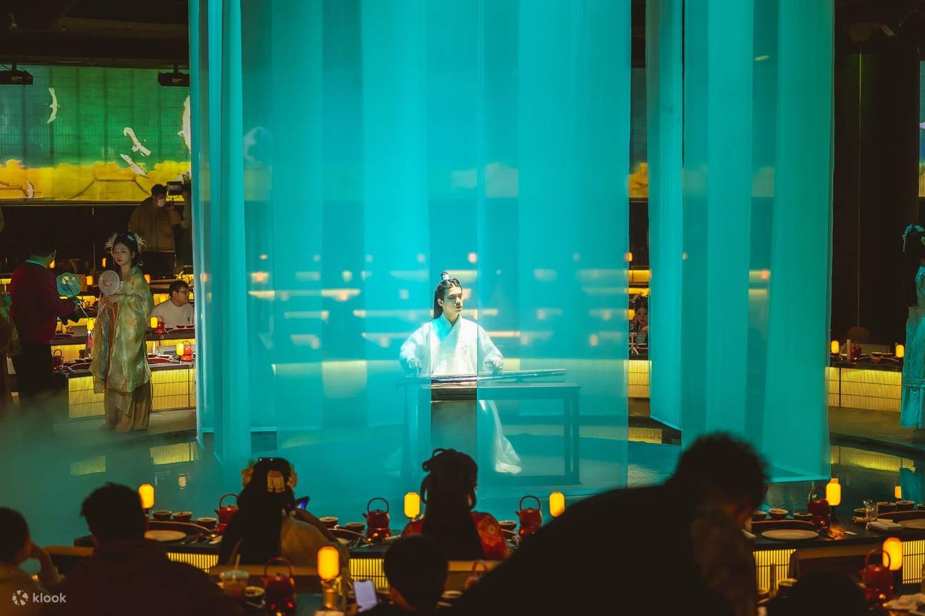 Duduk di meja, pemain dengan tekun memainkan Guqin, dikelilingi oleh tirai tipis yang menciptakan suasana tenang dan elegan.