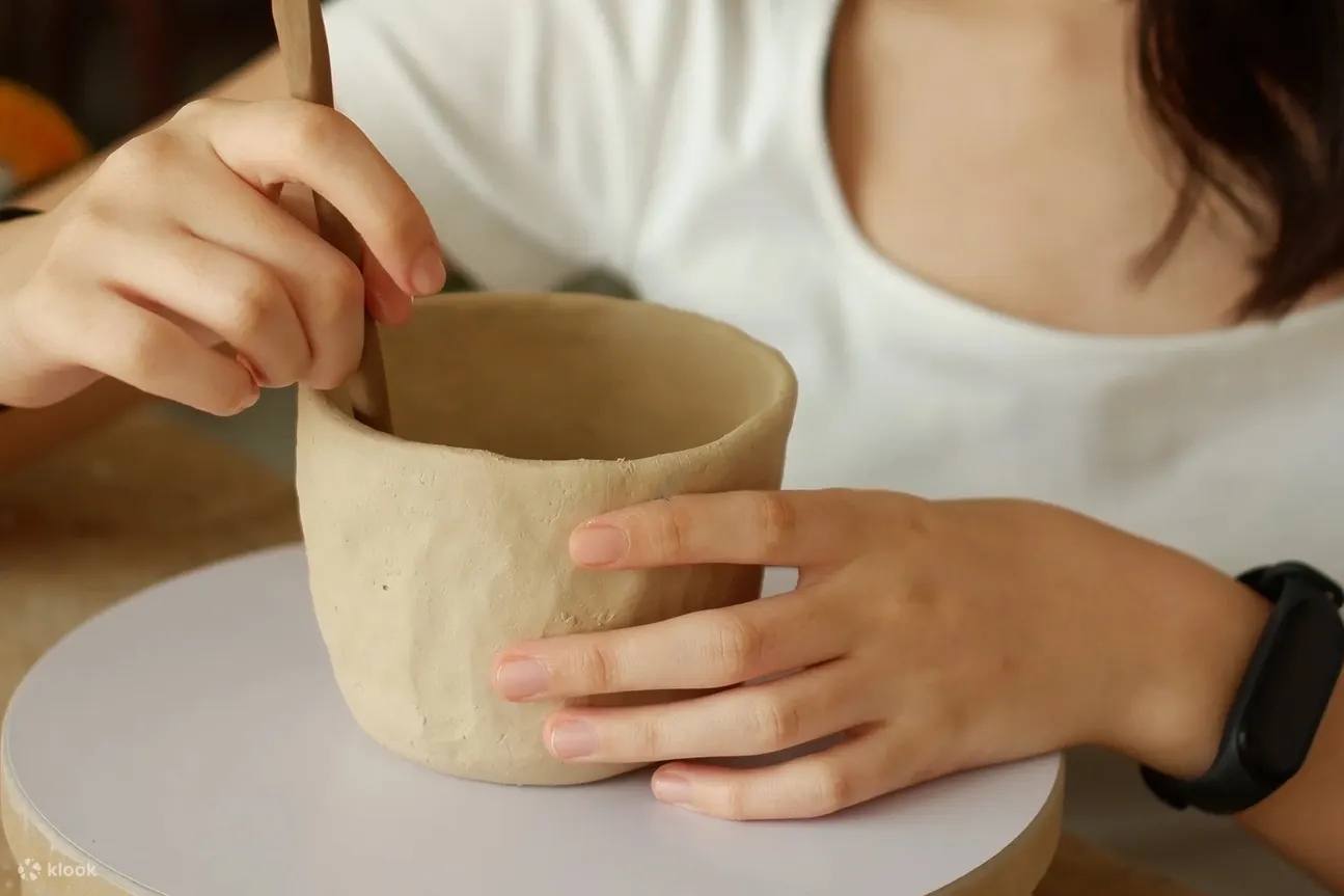 Person molding a clay mug with a tool