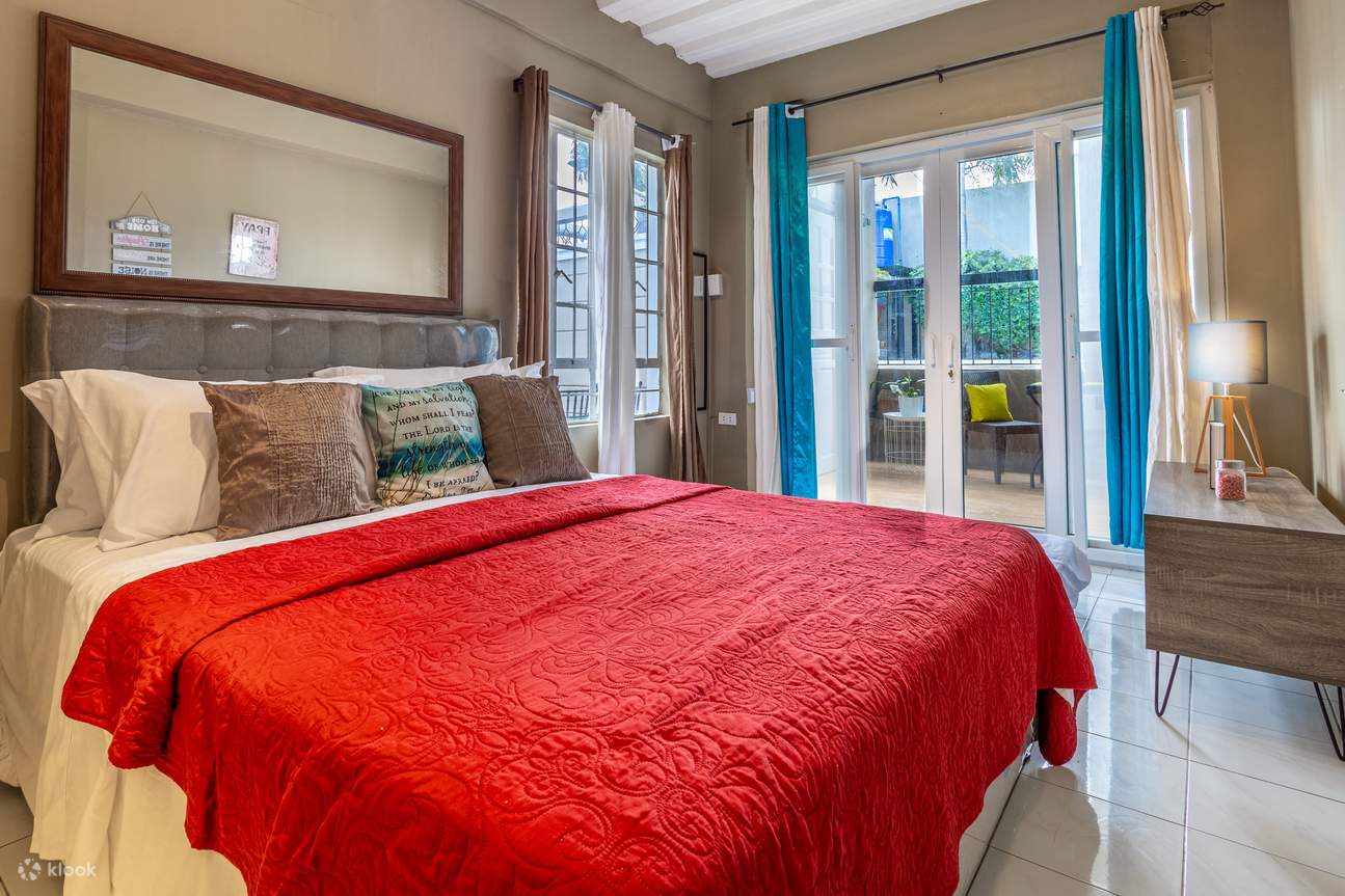 Спальня с красной кроватью на фоне белой стены и окном с синими шторами