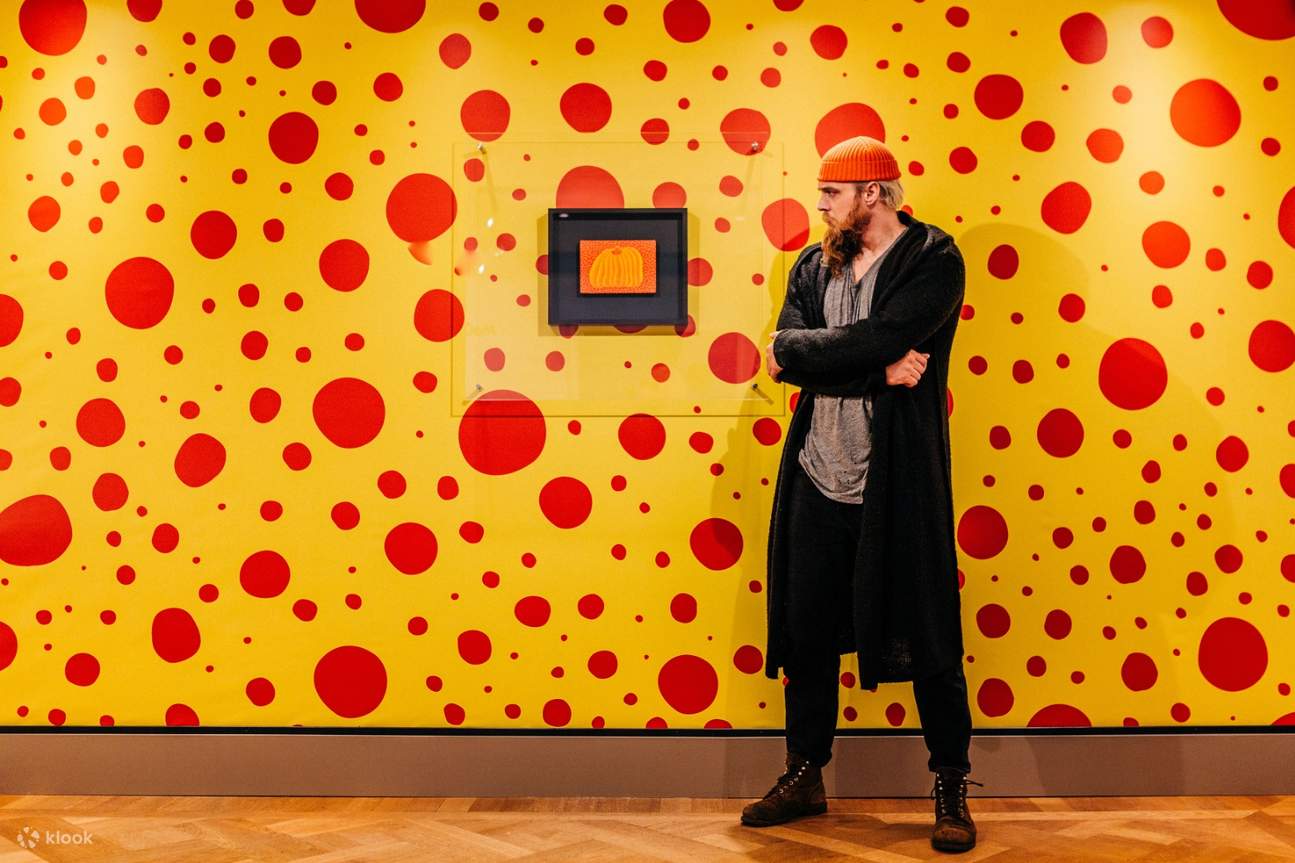 un hombre frente a una exhibición de arte con una pared punteada de fondo