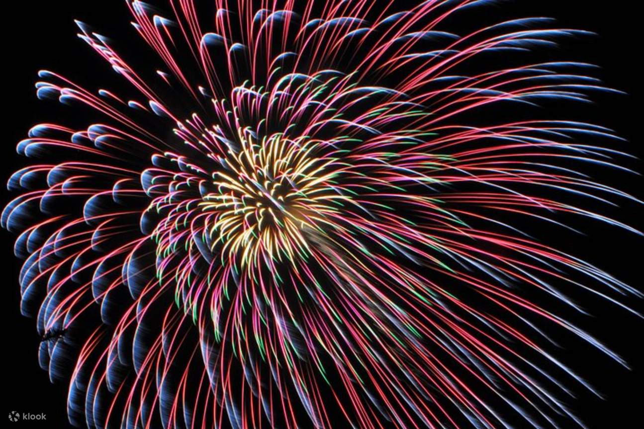 Brilliant fireworks illuminate the night sky, casting vibrant colors over the Pacific
