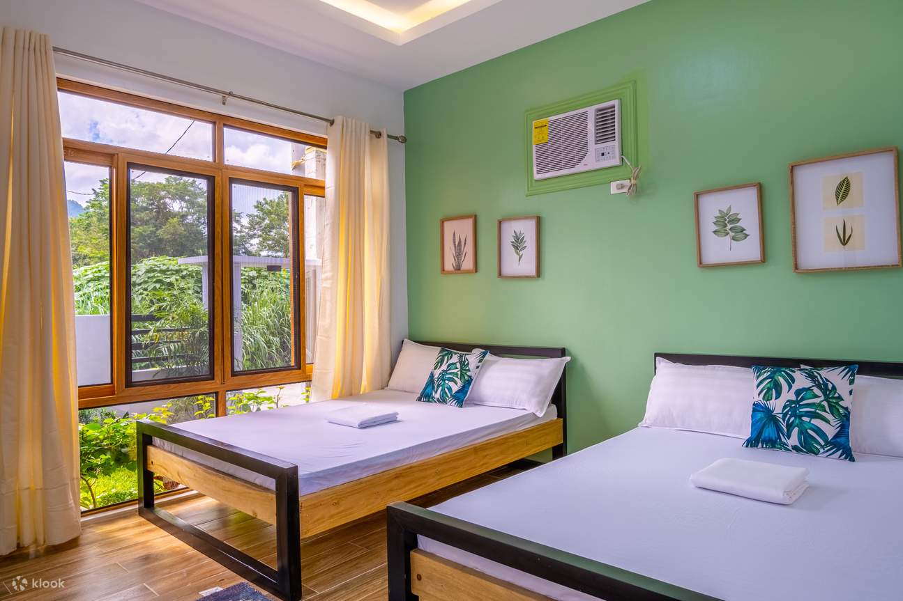 Dua tempat tidur di kamar tidur dengan dinding hijau dan jendela besar yang memungkinkan cahaya alami masuk