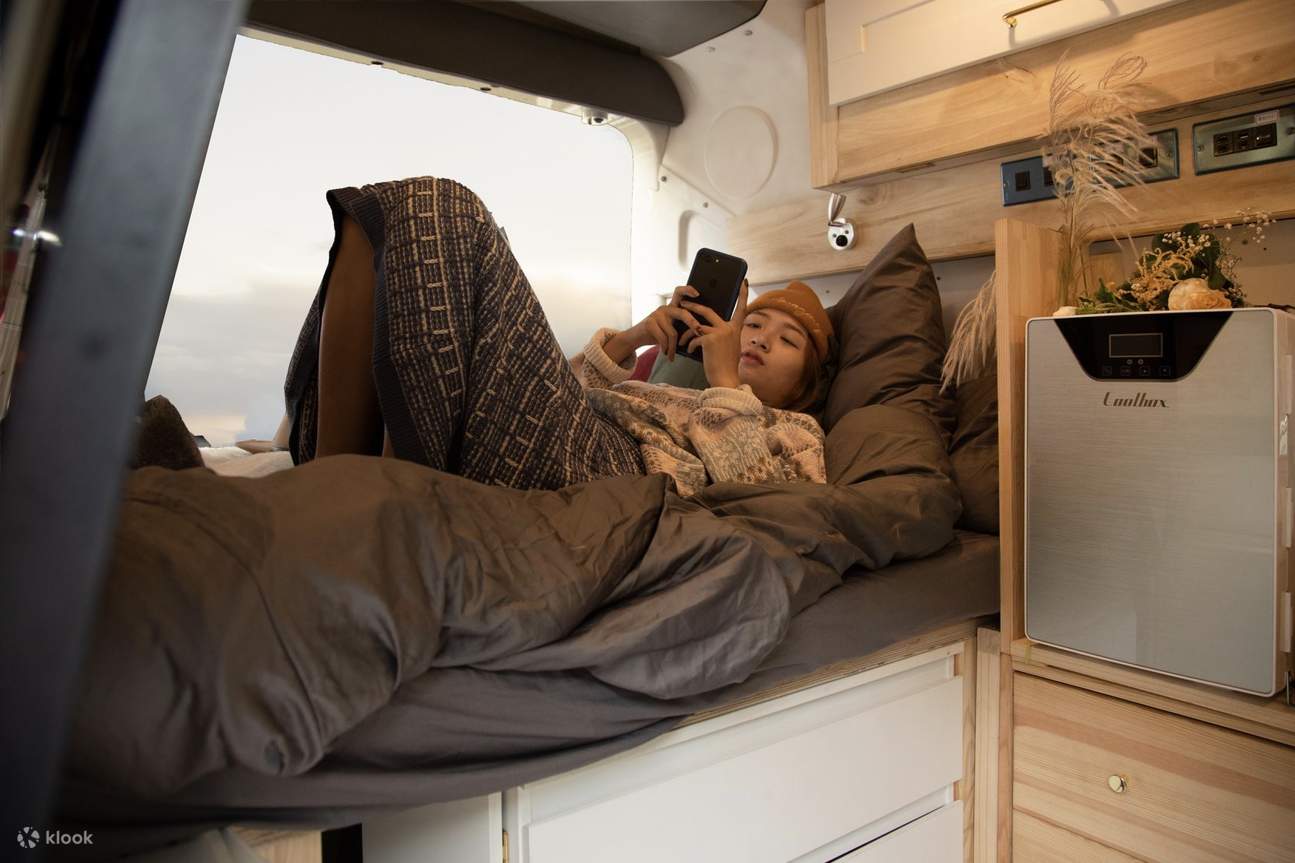 一位露營者躺在舒適的露營車裡滑手機
