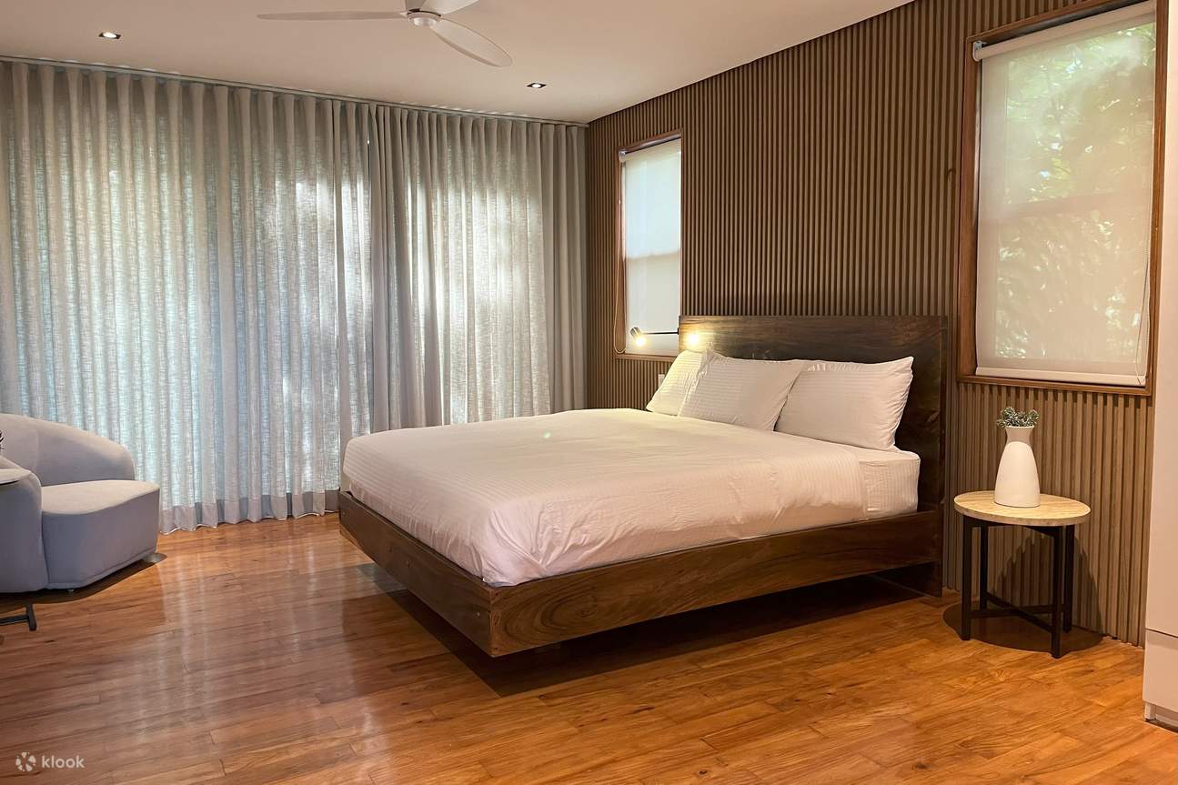 Letto king-size in una camera da letto con tende bianche e pannelli di legno sulla parete