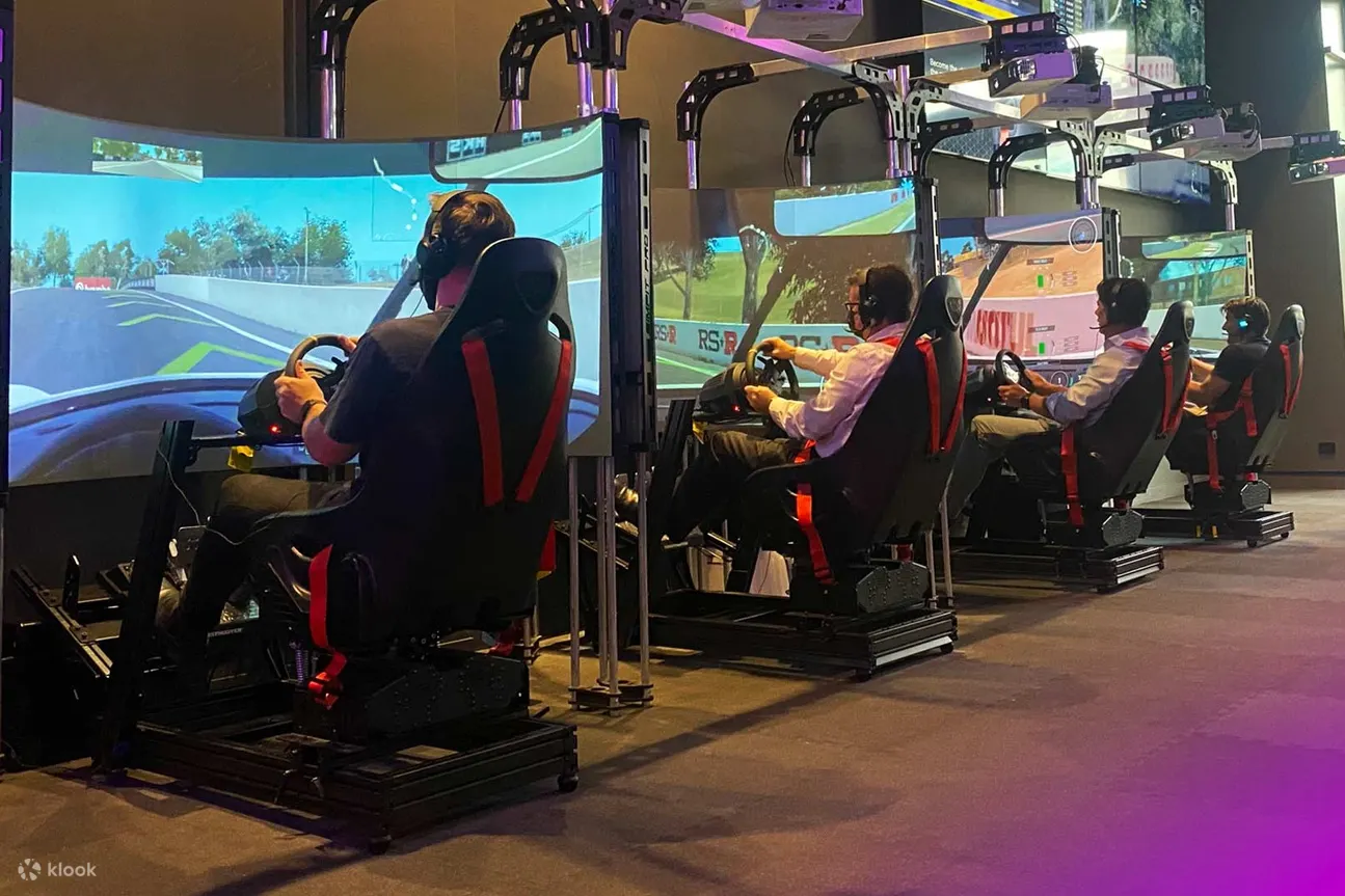 图片展示了几个人坐在高科技模拟器上体验赛车游戏，模拟器前配有大屏幕，环境显得现代化且专业。