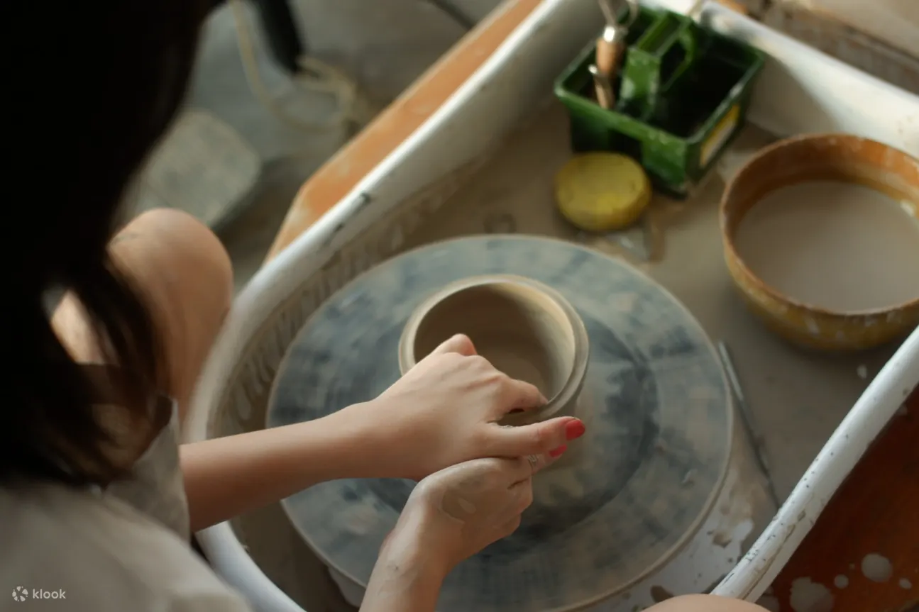 Person working on a pottery wheel and forming a mug