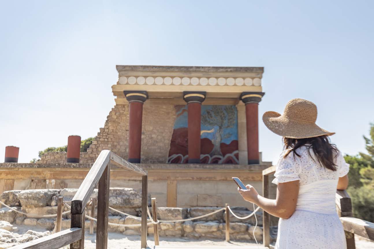 Un visitante escucha la audioguía mientras está de pie frente a las icónicas columnas rojas del Palacio de Knossos