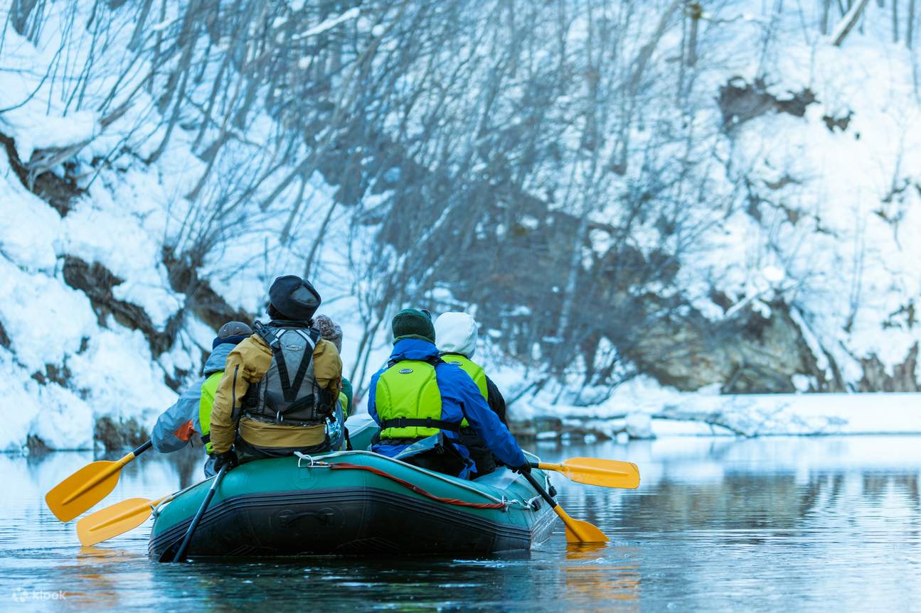 People row the raft next to the mountain covered by snow