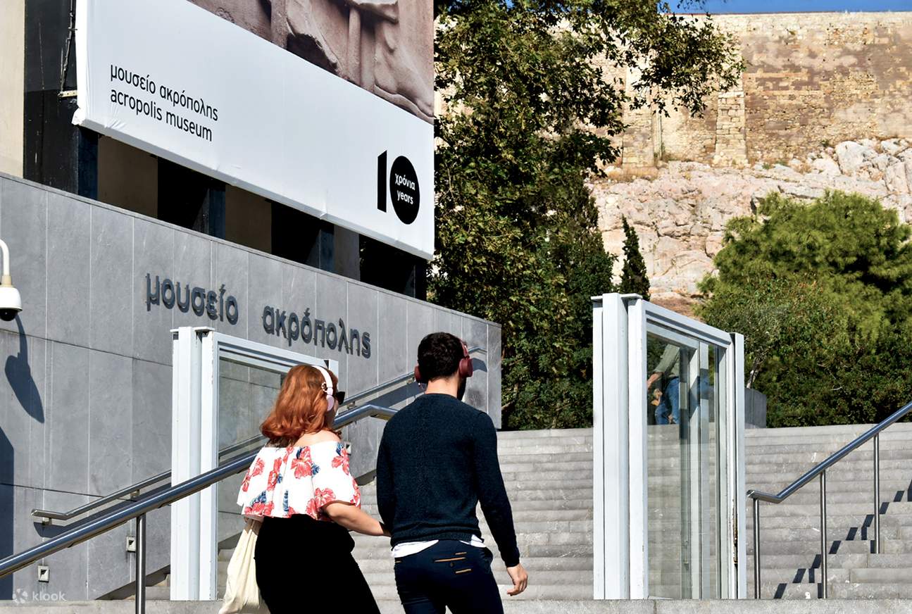 Dos visitantes caminando fuera del museo, rodeados de vegetación y arquitectura moderna