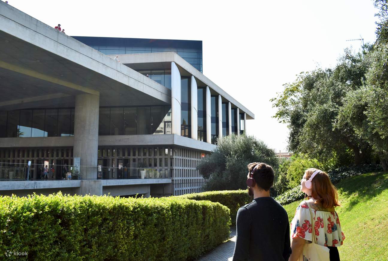 Dos visitantes observando el diseño exterior del Museo de la Acrópolis