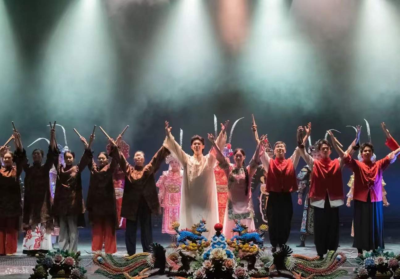 Los actores, vestidos con trajes tradicionales, extienden sus brazos hombro con hombro, con brillantes decoraciones de dragón y fénix en el frente del escenario, y una luz tenue que muestra la calidez del cierre del telón.