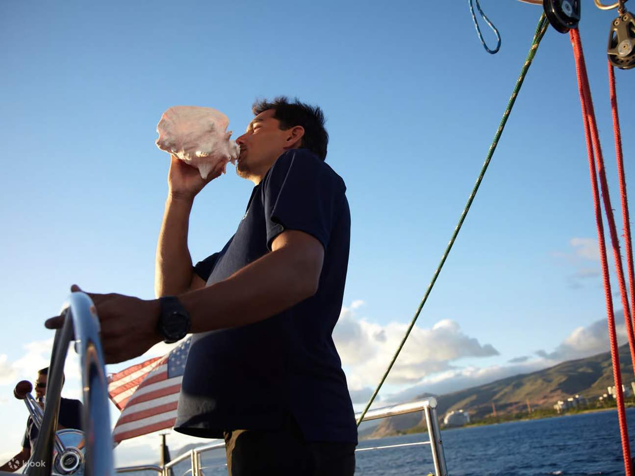 Escuche el llamado de la caracola mientras un huésped la sopla mirando al horizonte oceánico.