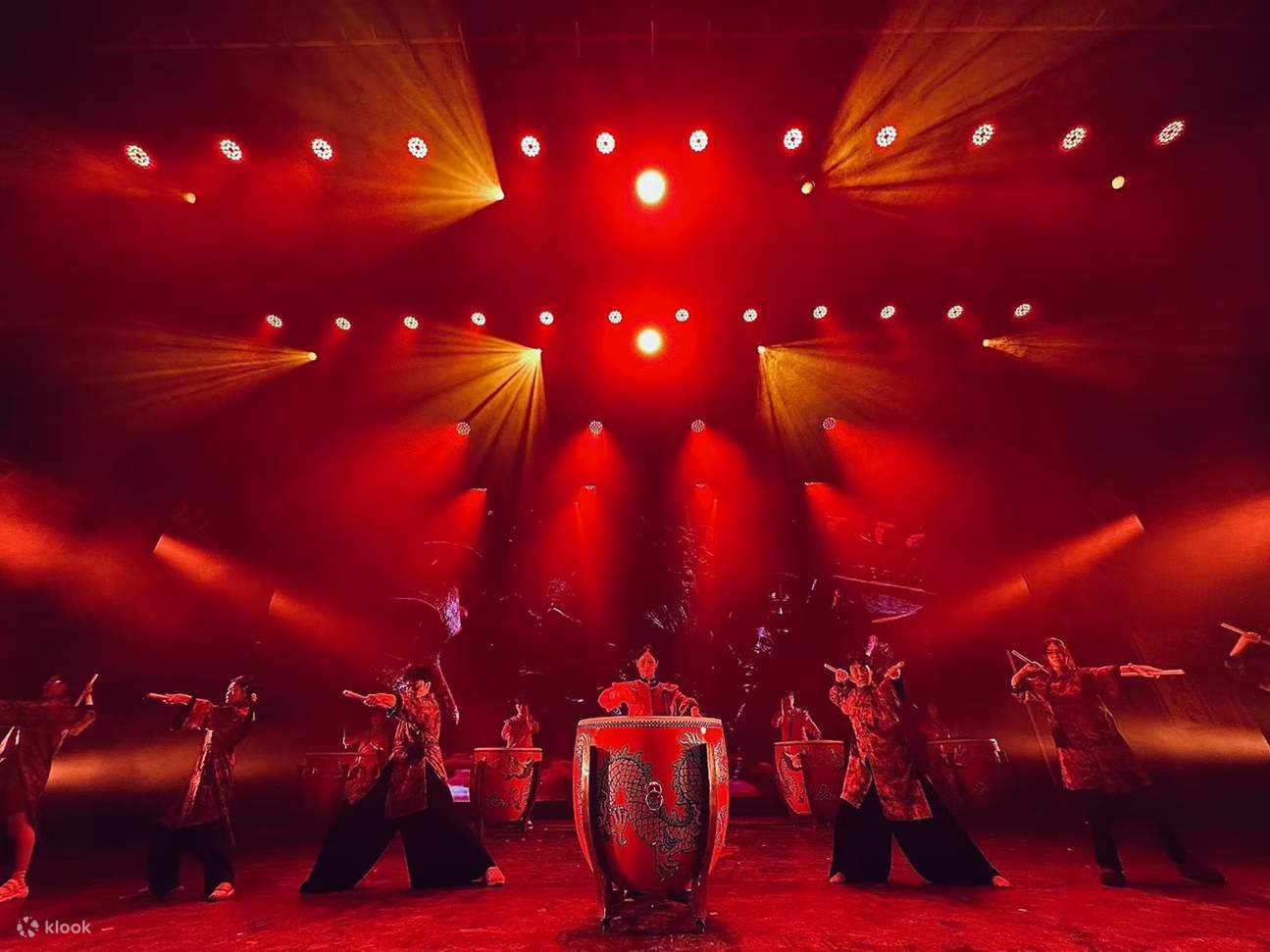 Die in rotes Licht getauchten, rot gekleideten Schauspieler trommeln, wobei sich Drachenmuster auf den Trommeln mit kraftvollen Bewegungen vereinen und die Bühne leidenschaftlich und erschütternd ist.