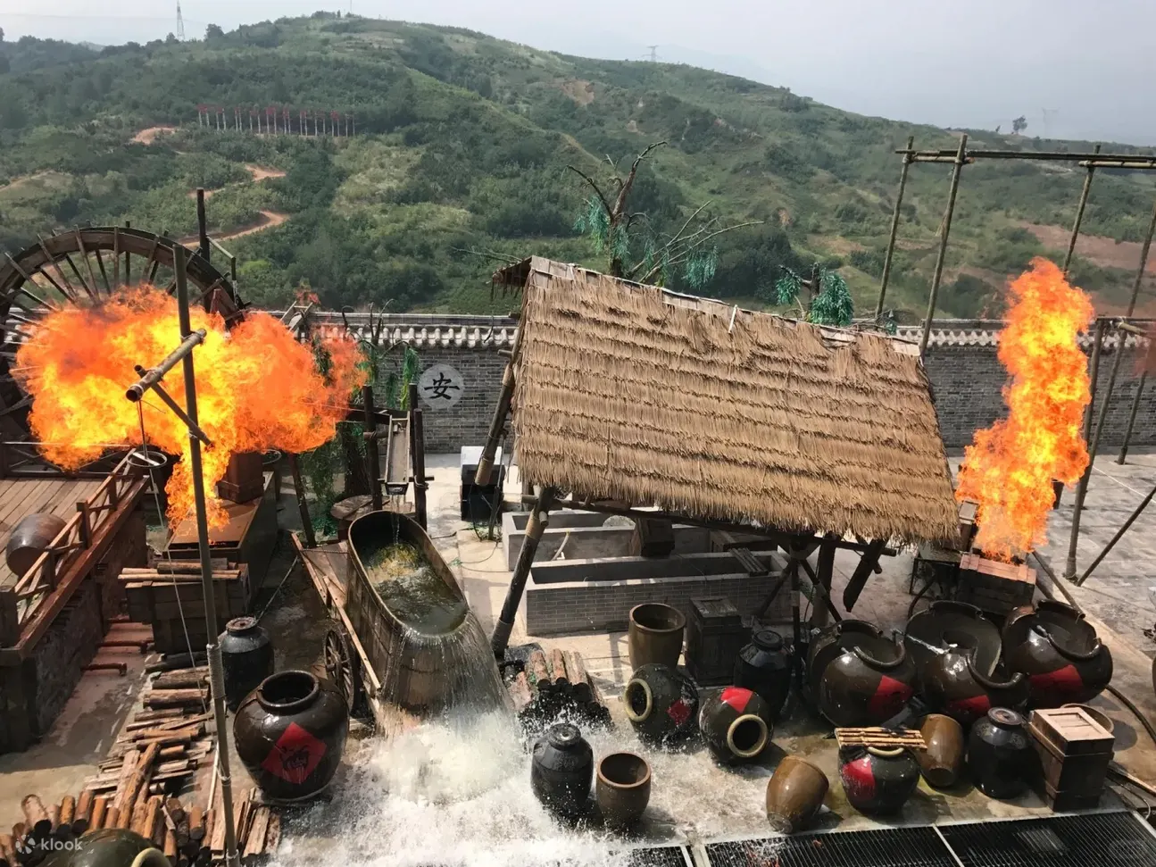 白鹿原影视城的实景演出场景，展现关中特色风貌：以茅草屋、大水车、酒坛等元素，还原传统酿酒作坊，熊熊火焰增添紧张刺激感，配合山水背景，营造出沉浸式的视听体验
