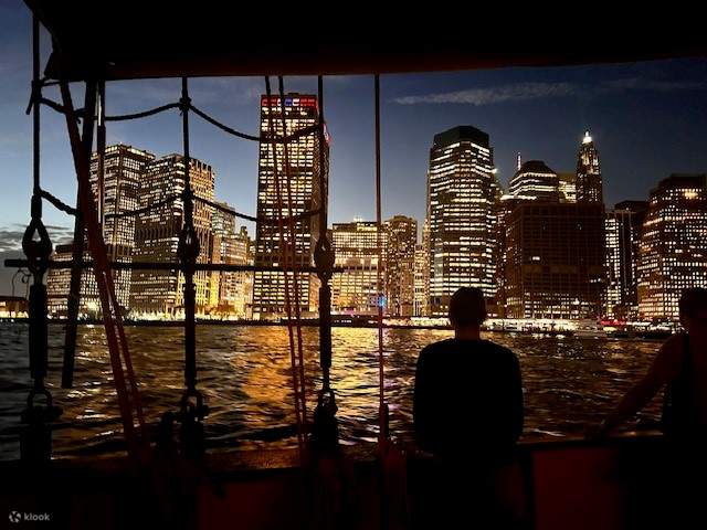 La silhouette de la ville se dresse au-delà de l'East River, ses lumières scintillant sur l'eau sous le ciel du soir.