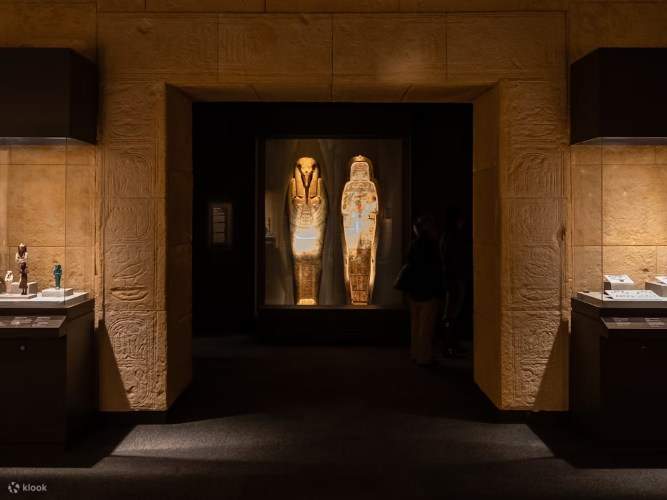 강렬한 조명 아래 상형문자와 미라 유물과 함께 전시된 고대 이집트 석관