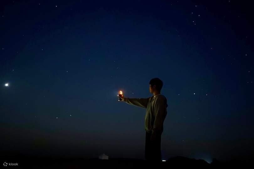 Eine Silhouette, die ein kleines Licht unter einem sternenübersäten Himmel hält – ein stiller Moment in der Nacht.