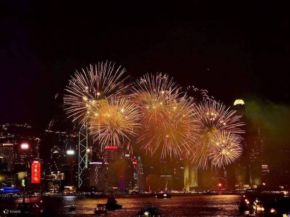 Bright golden fireworks burst above the illuminated Hong Kong skyline, reflecting on the water during a celebration for Hong Kong National Day 2025.